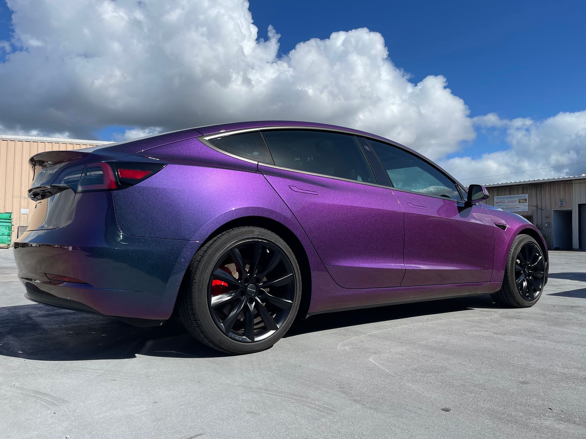 A purple tesla model 3 is parked in a parking lot.