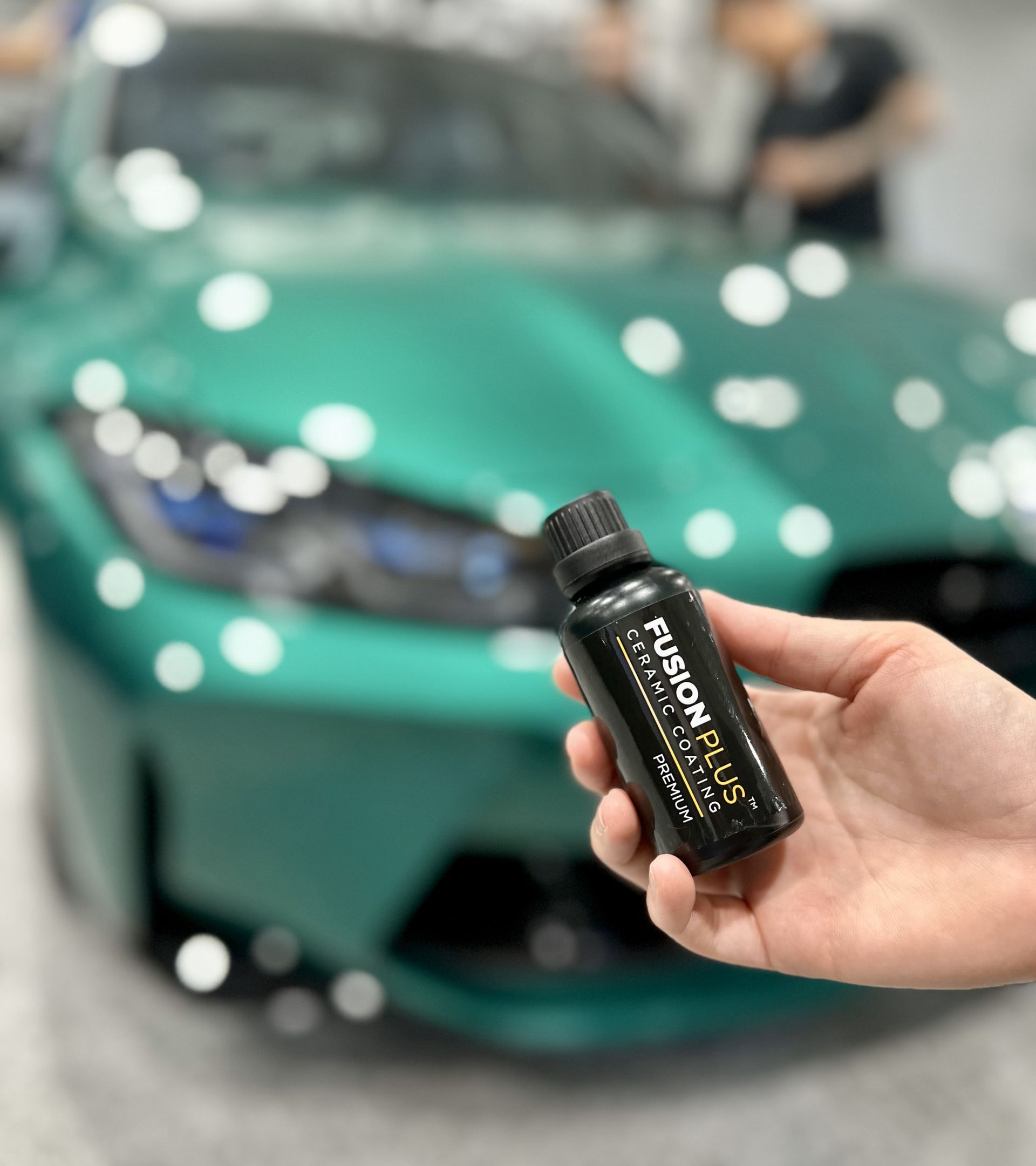 A person is holding a bottle of phantom gloss in front of a green car