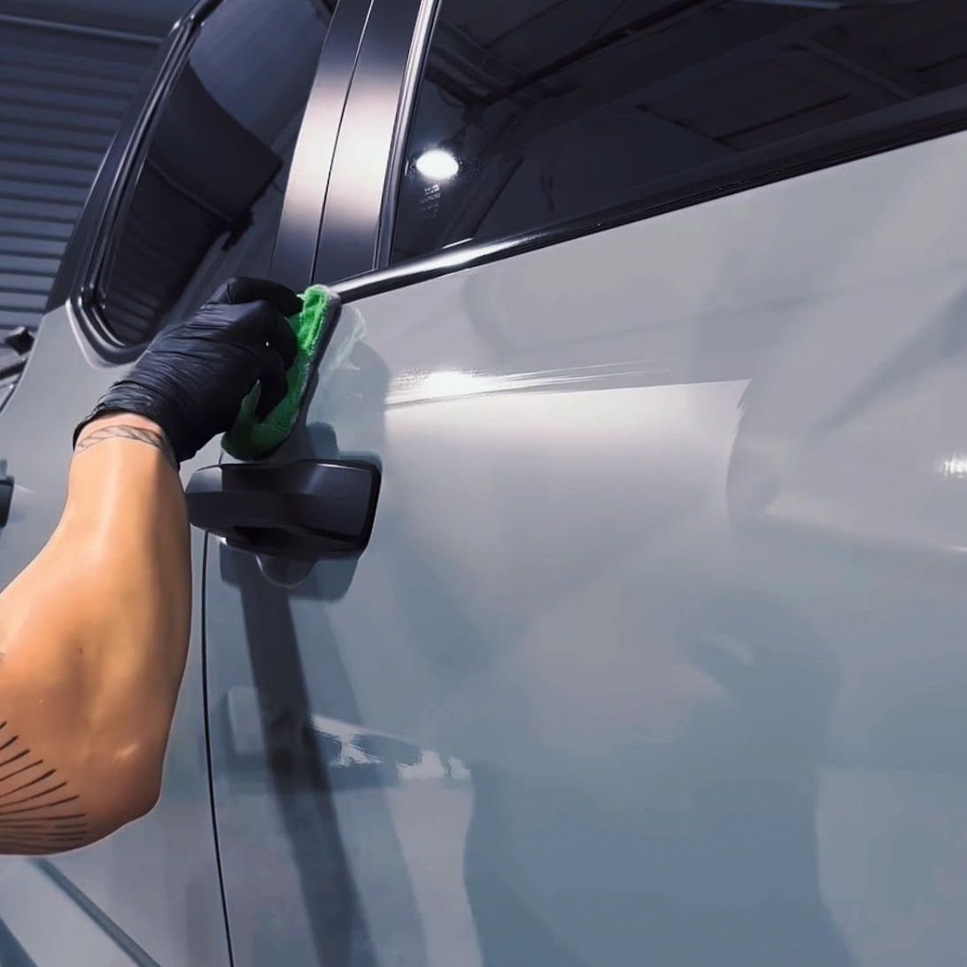A person cleaning a car door with a green sponge