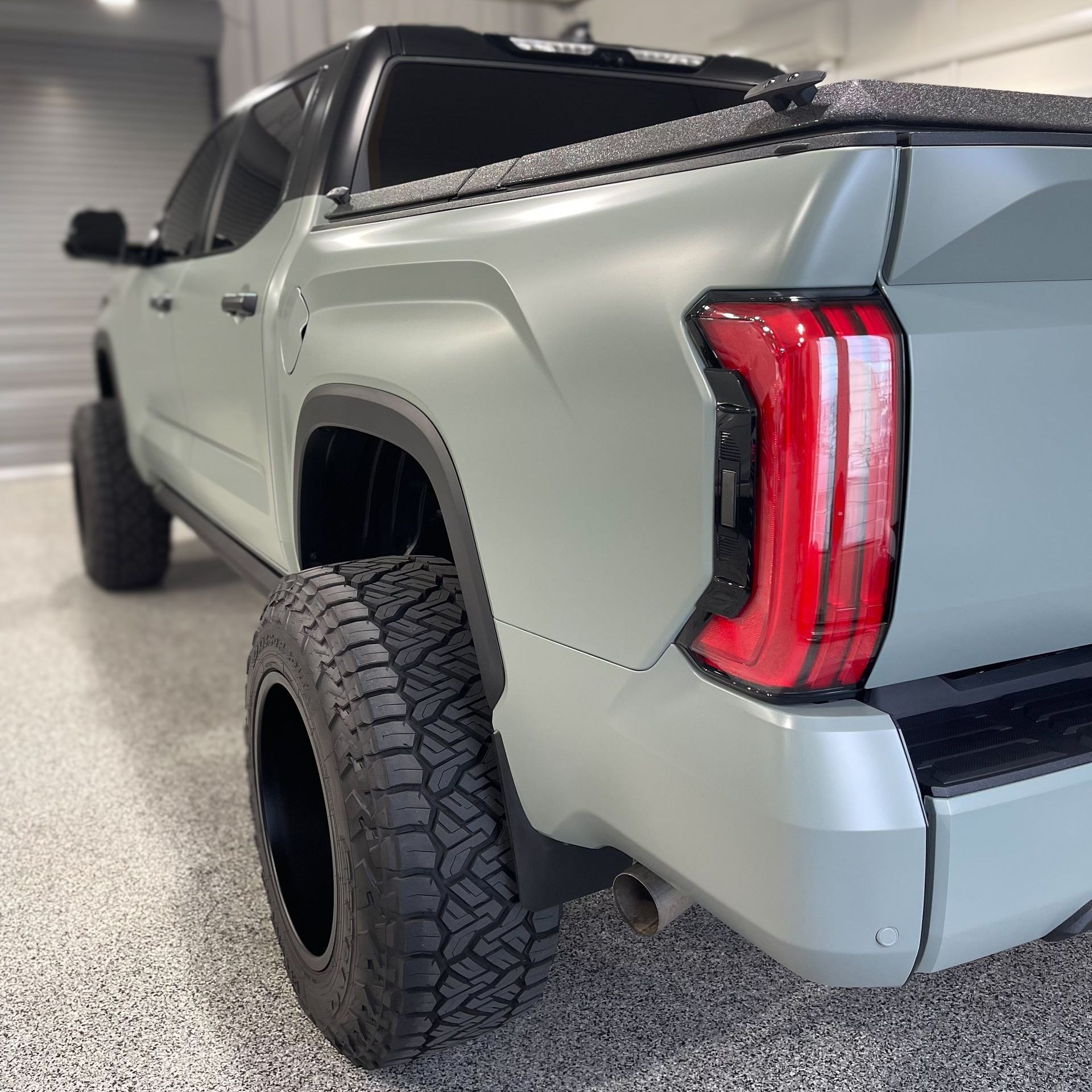 A grey truck with a red tail light is parked in a garage
