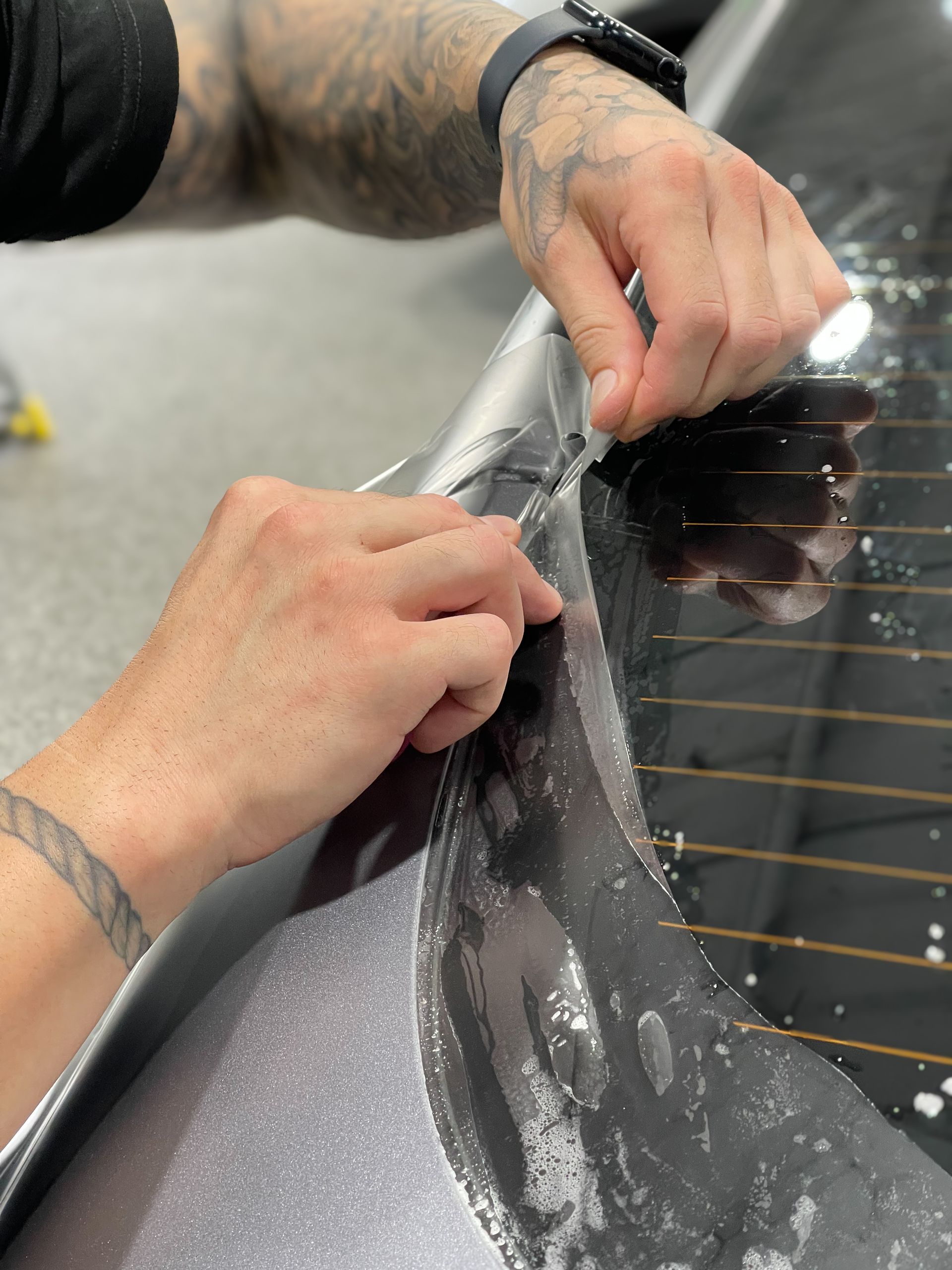A man is cutting a piece of plastic on the back window of a car.