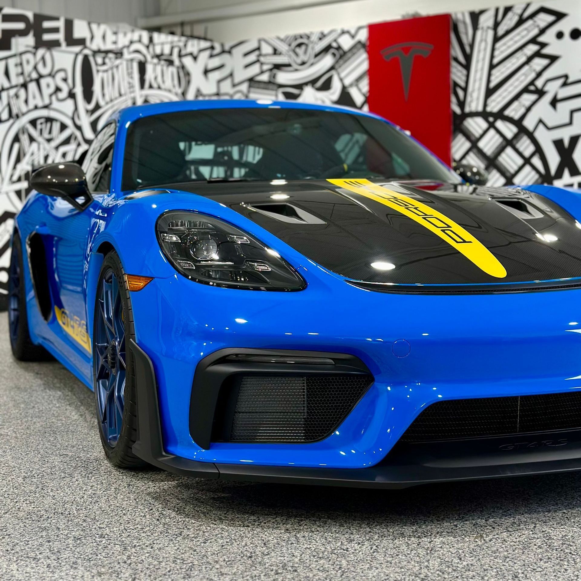 A blue sports car is parked in front of a wall with graffiti on it
