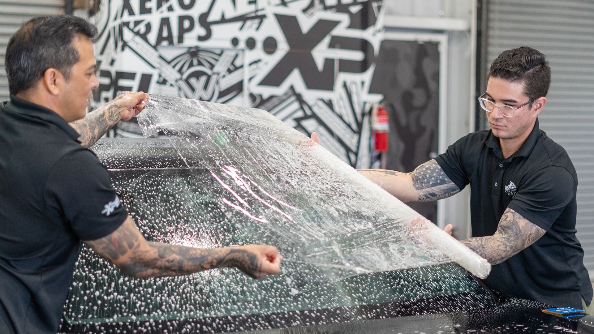 A man is cleaning the windshield of a black car.