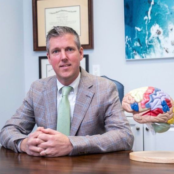 Dr. Jonathan A. Beatty sits at a desk in front of a model of a brain