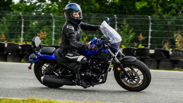 A person in full protective gear rides a blue motorcycle on a track lined with tire barriers.