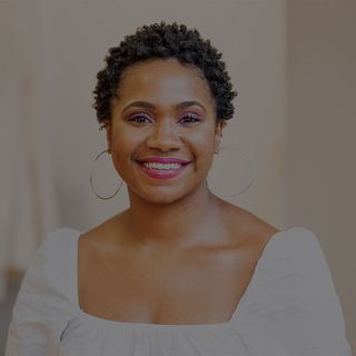 A smiling Black woman with short curly hair wearing a white top and large hoop earrings.