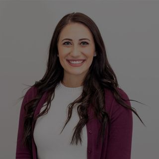 Smiling woman with long dark hair, wearing a white top and burgundy cardigan, against a neutral background.