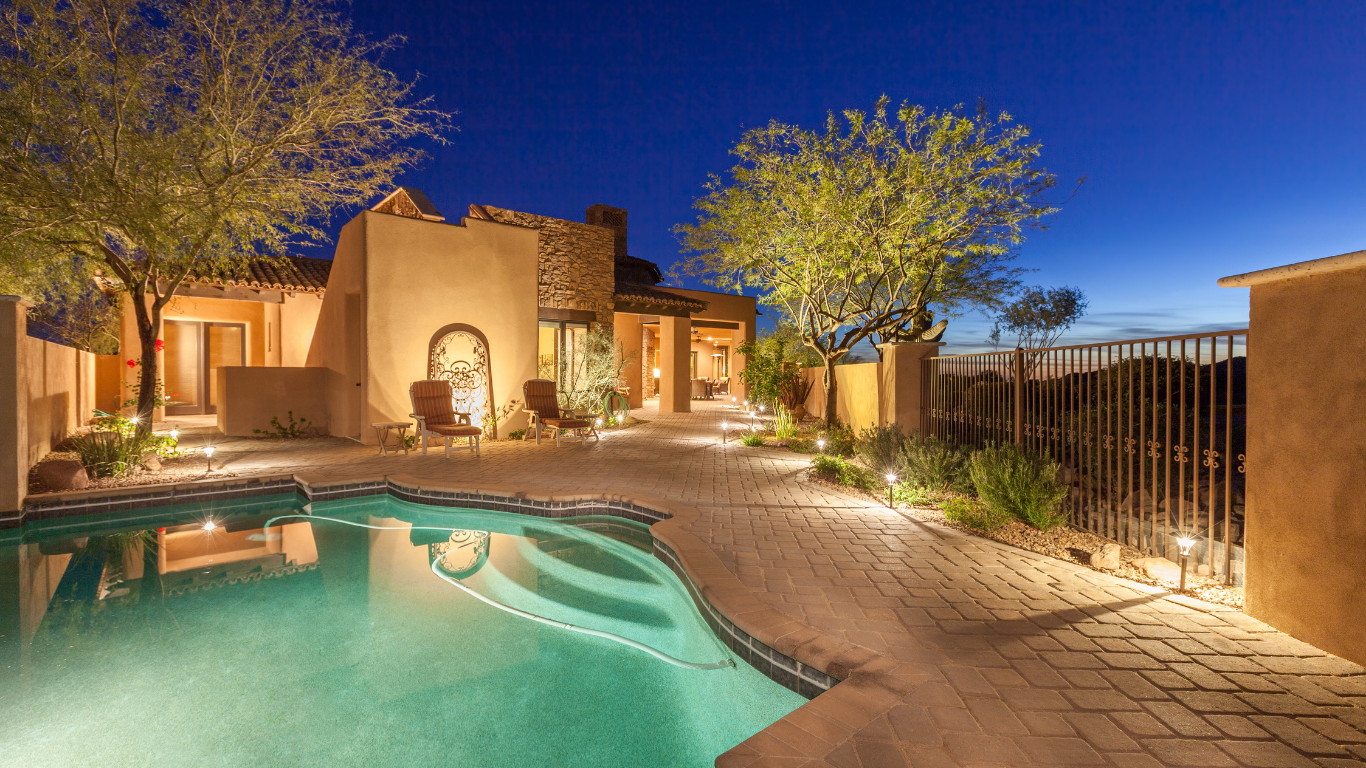 A large swimming pool is in the backyard of a house at night.