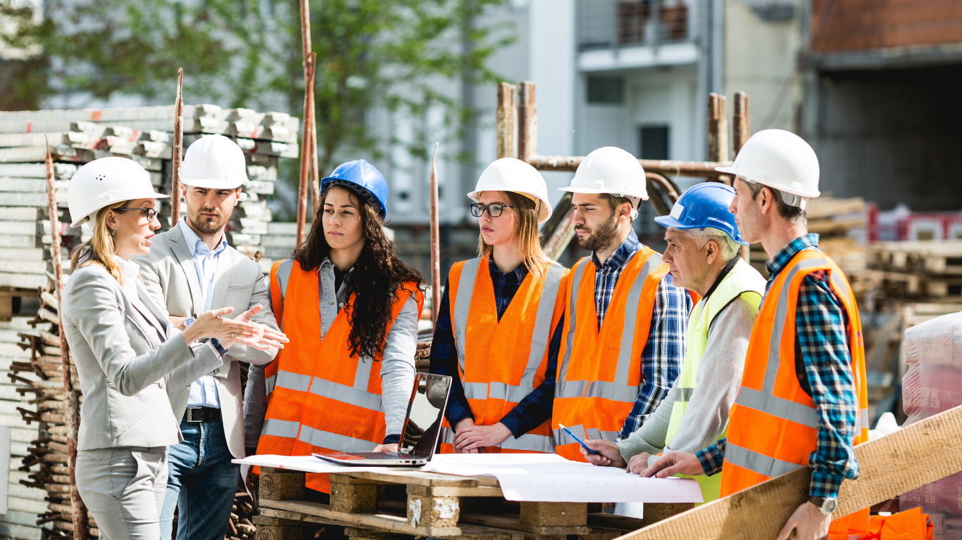 A group of construction workers are standing around a woman on a construction site.