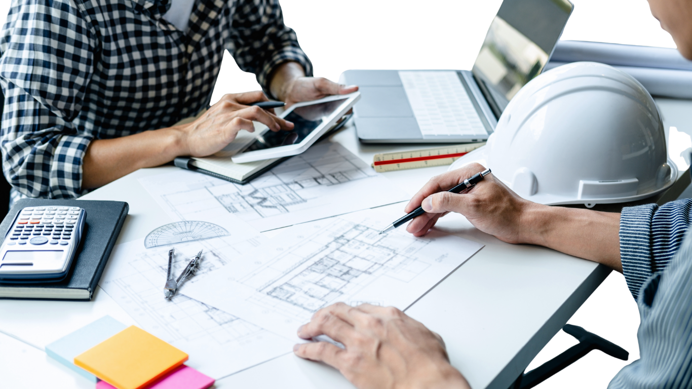 Two men are sitting at a table looking at a blueprint.