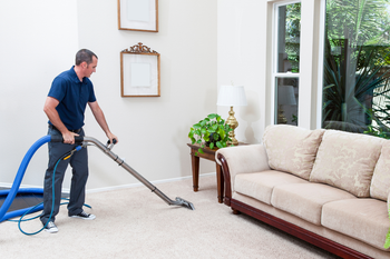 A man is cleaning the carpet in a living room with a vacuum cleaner.