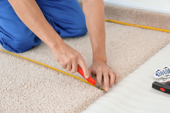 A man is measuring a piece of carpet with a tape measure.
