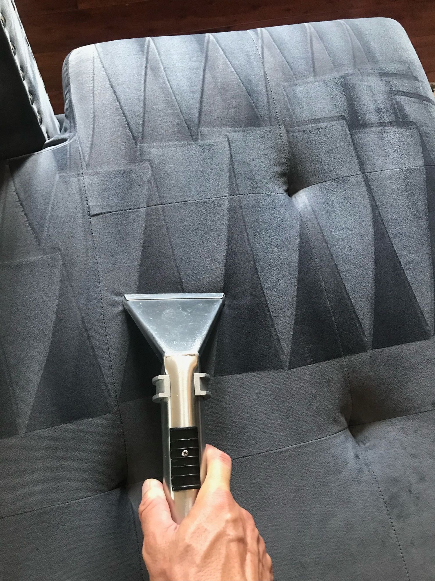 A person is cleaning a couch with a vacuum cleaner.