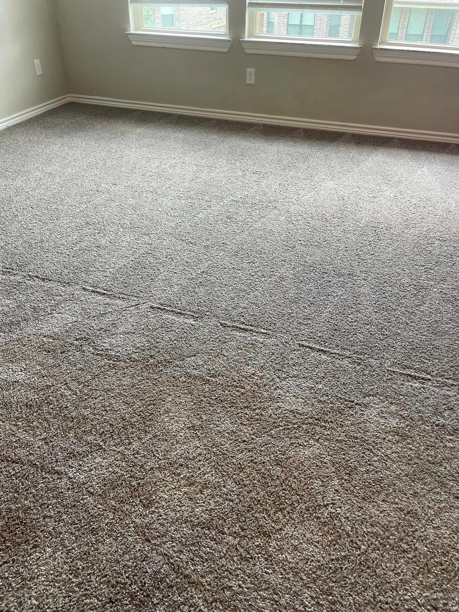A living room with a large carpeted floor and three windows.