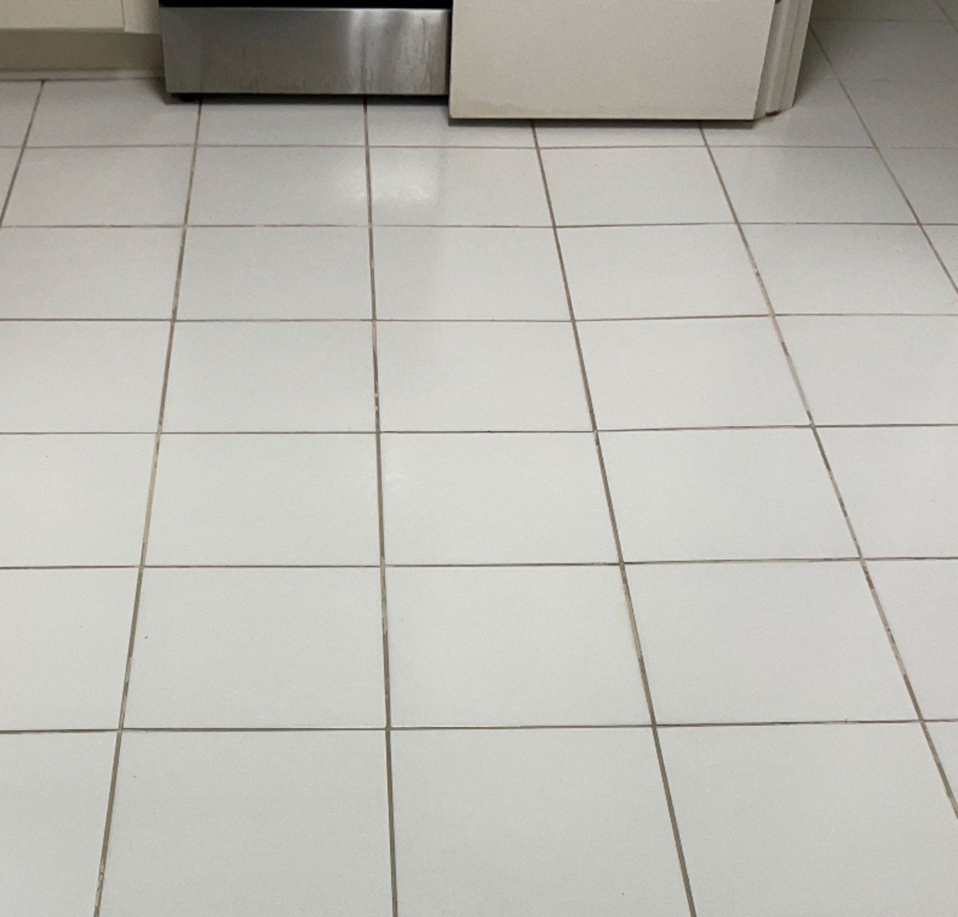 A kitchen floor with white tiles and a stainless steel refrigerator