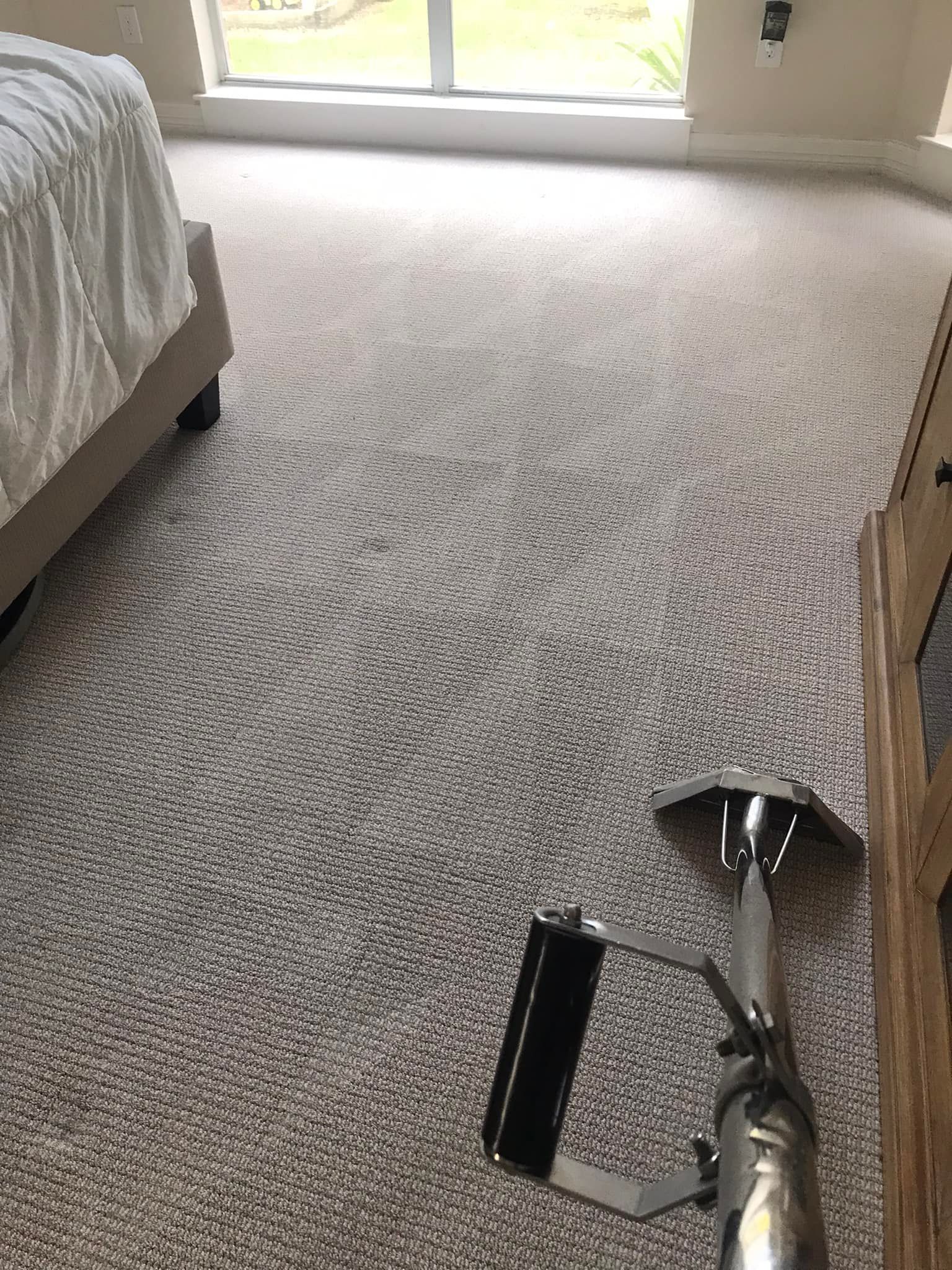 A vacuum cleaner is sitting on a carpet in a bedroom next to a bed.