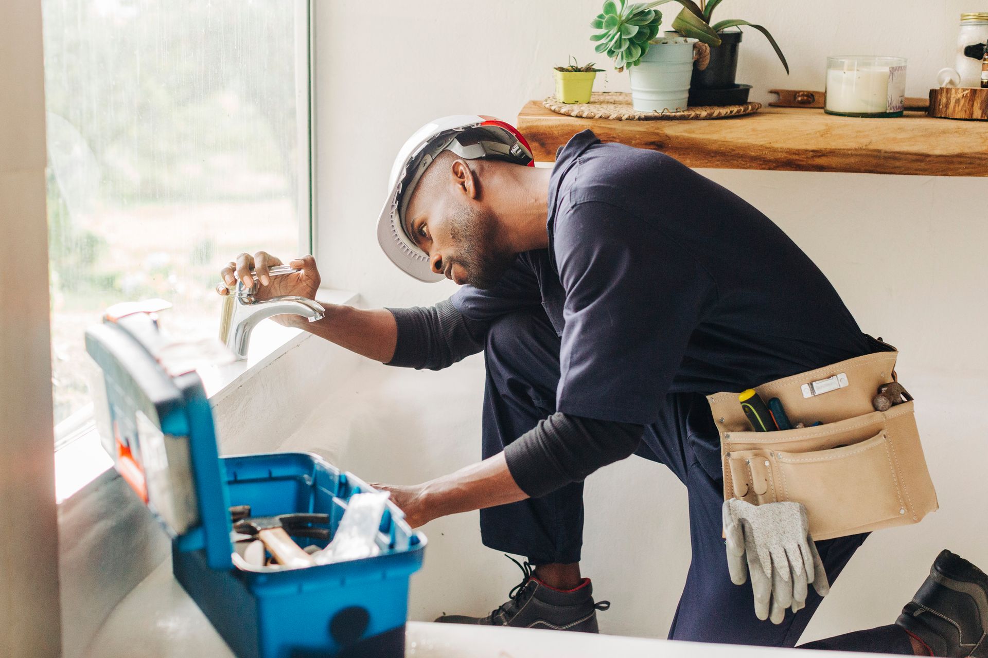 Man in hard hat and tool belt fixing window.