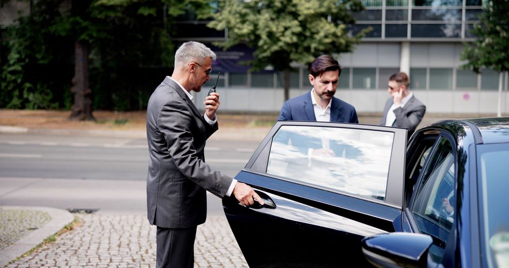 A man in a suit is opening the door of a car.