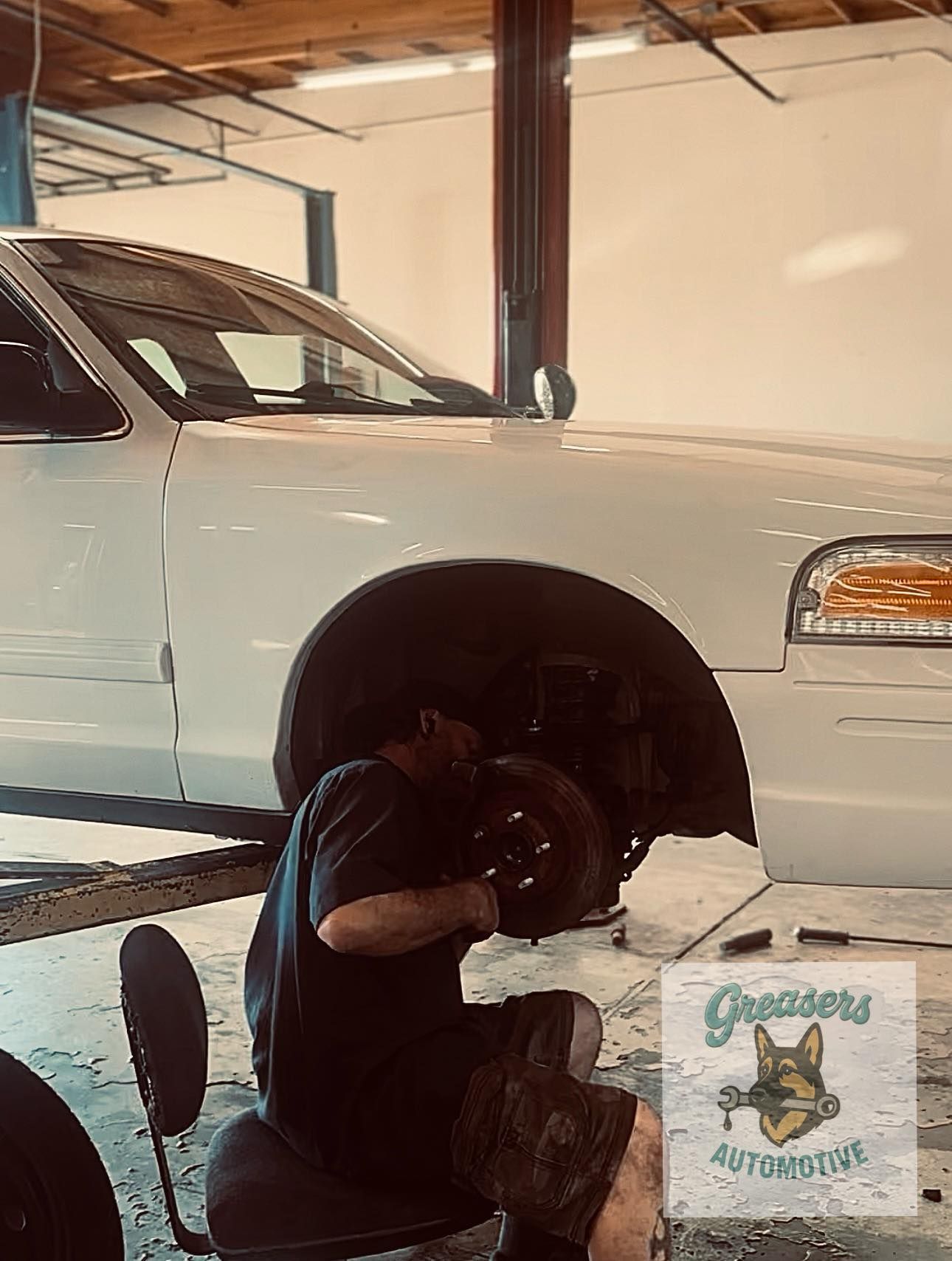 Mechanic working on a white car's front tire in an auto shop | Greasers Automotive