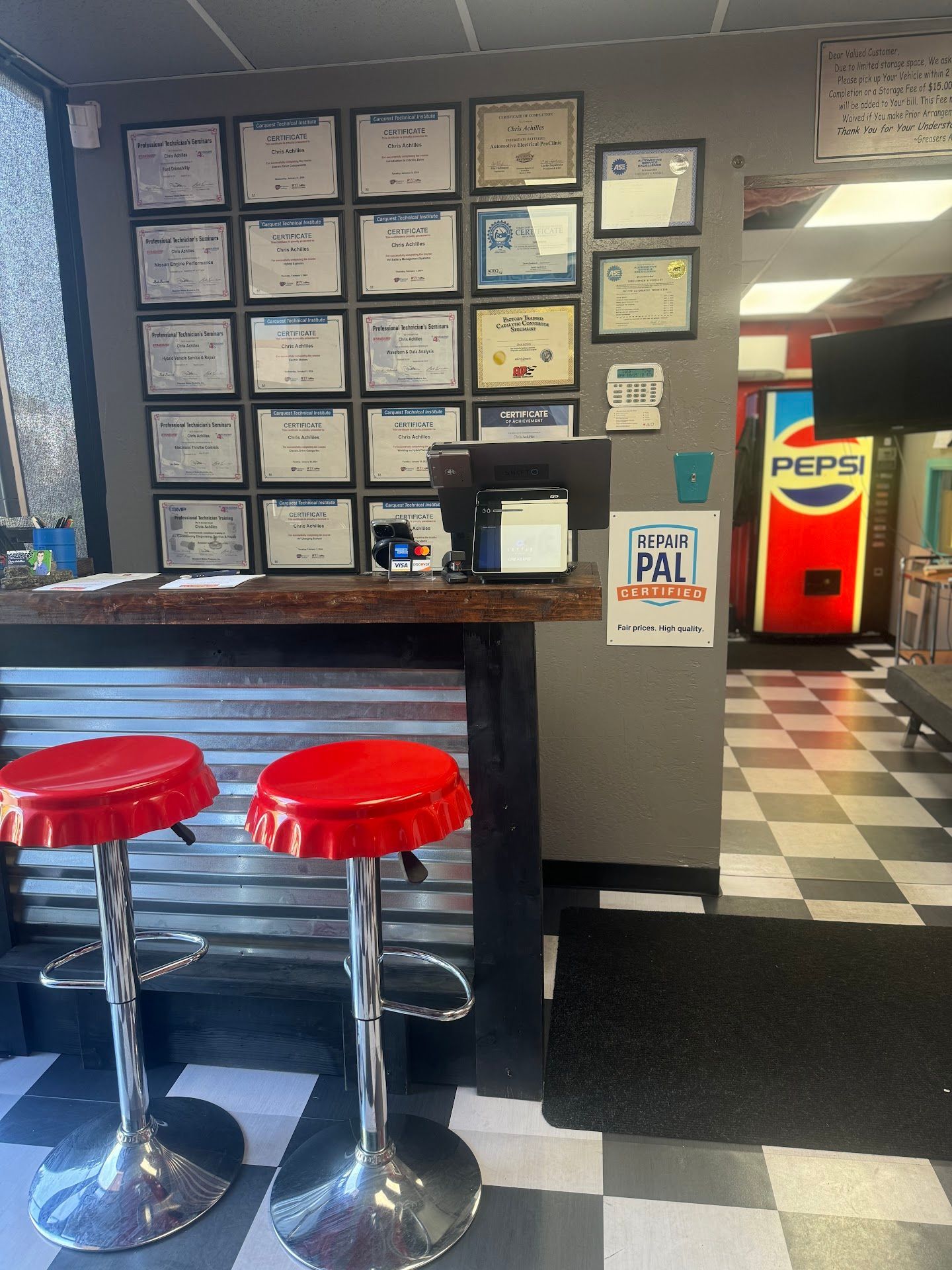 Two Red Stools at a Counter, Certificates on Wall, Pepsi Machine in Background | Greasers Automotive
