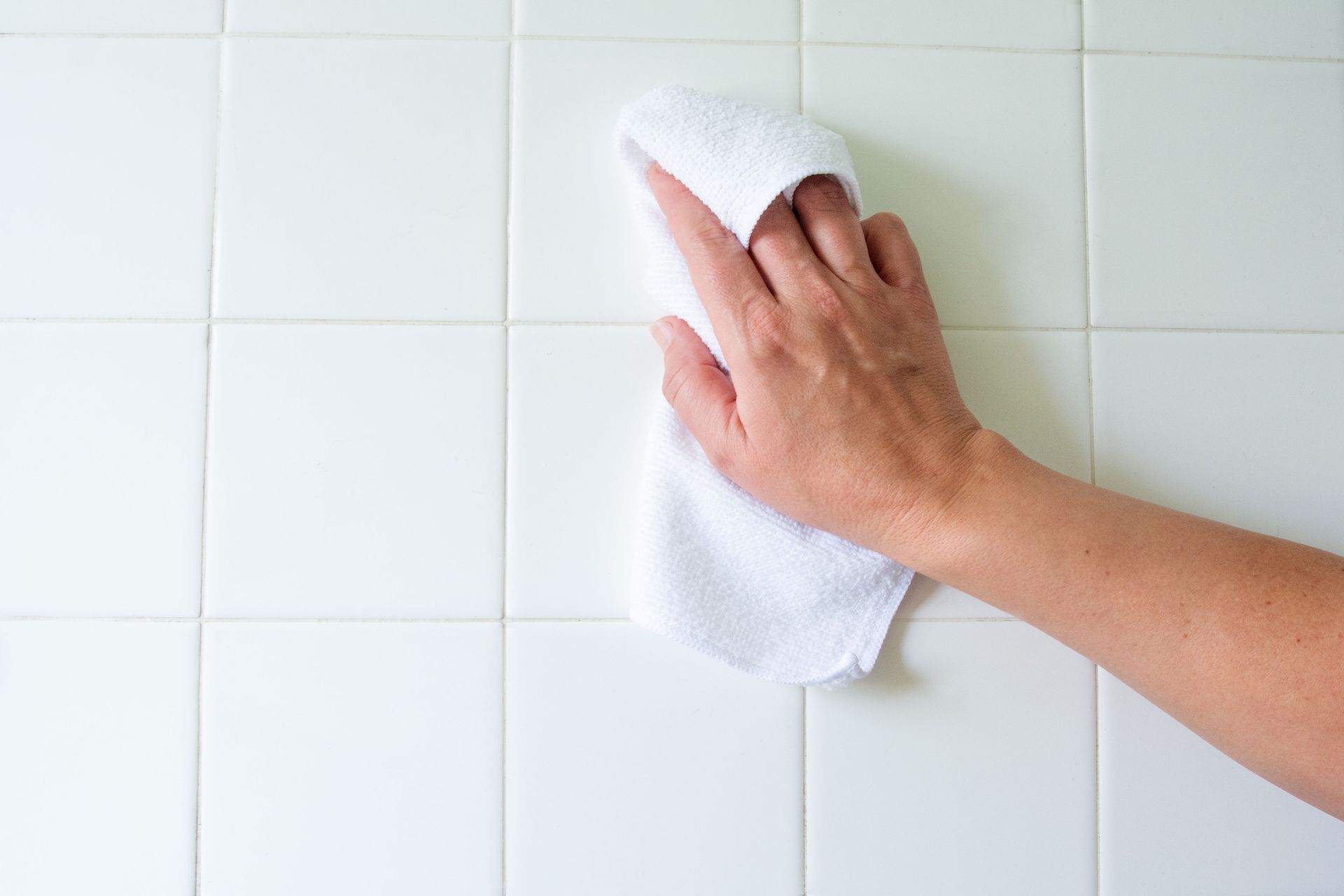 A person is cleaning a white tile wall with a towel.