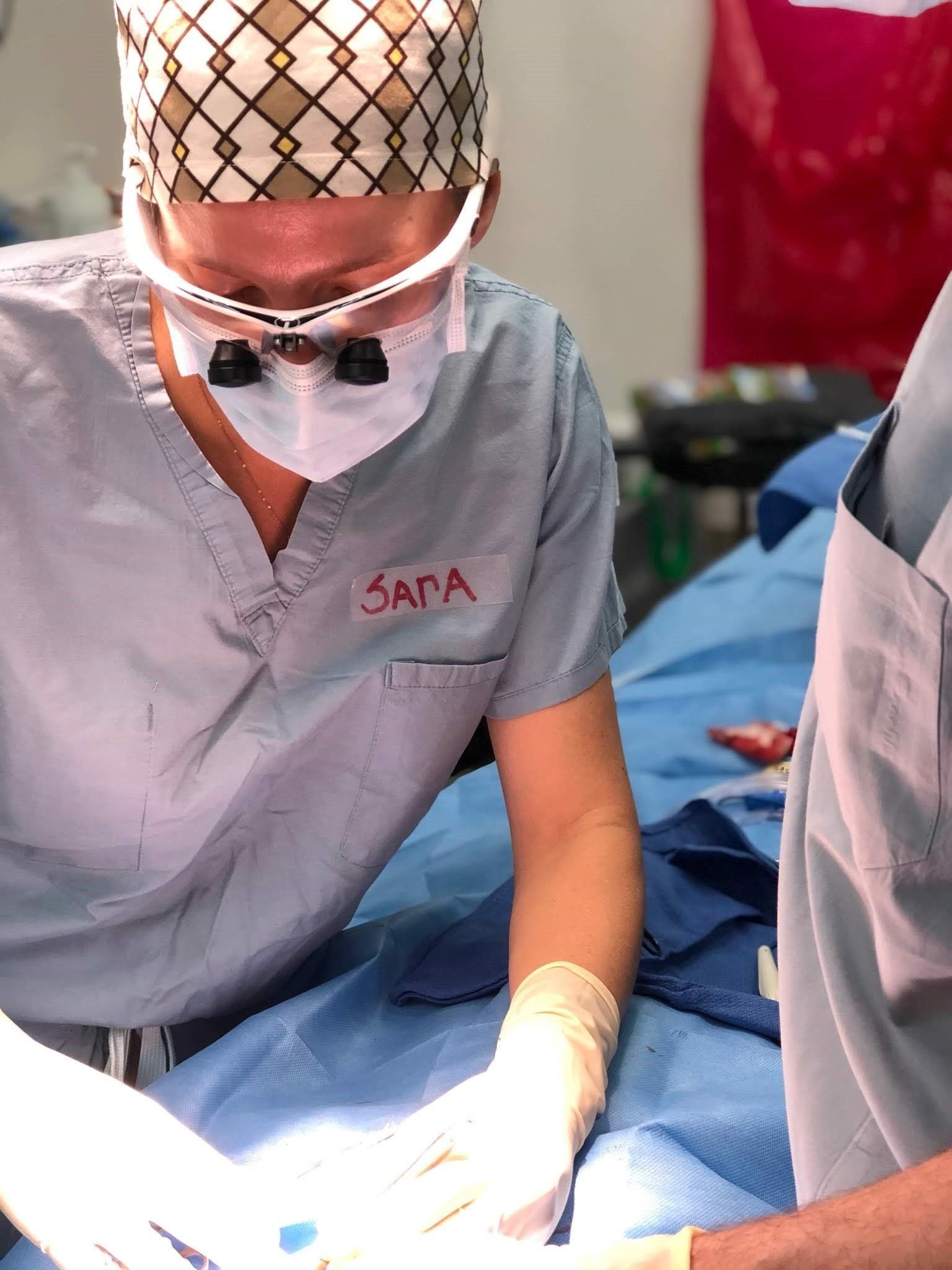 A surgeon wearing a scrub top with the name sara on it