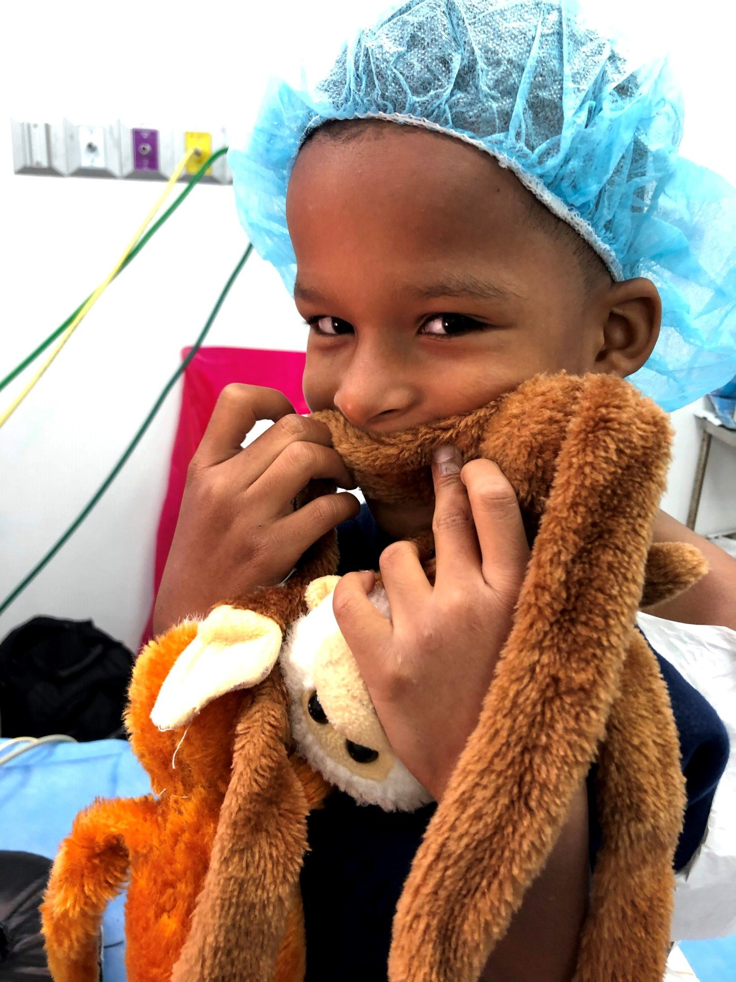 A child wearing a surgical cap is holding a stuffed animal