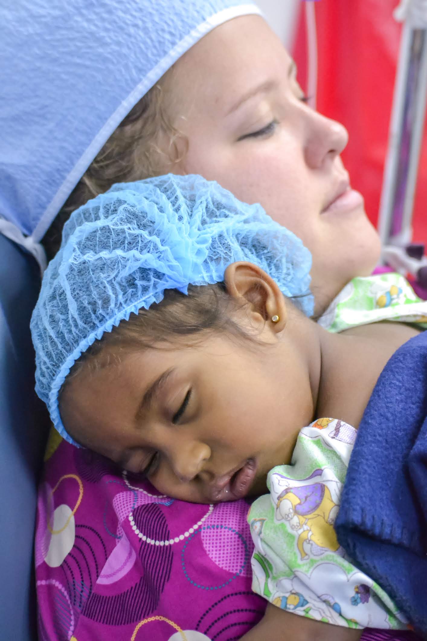 A woman in a surgical cap is holding a baby in her arms
