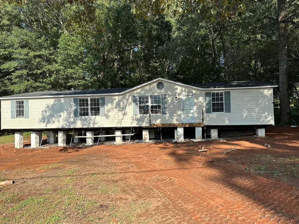 A mobile home is sitting on stilts in the middle of a dirt field.