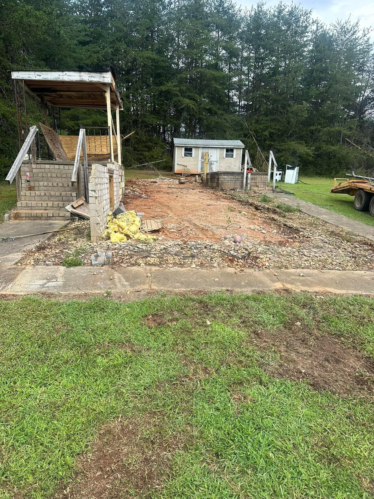 A dirt road leading to a house with a trailer in the background.