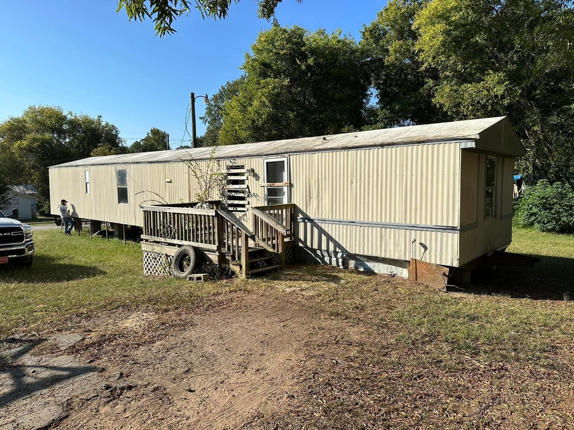 A mobile home with stairs and a deck is parked in a dirt field.