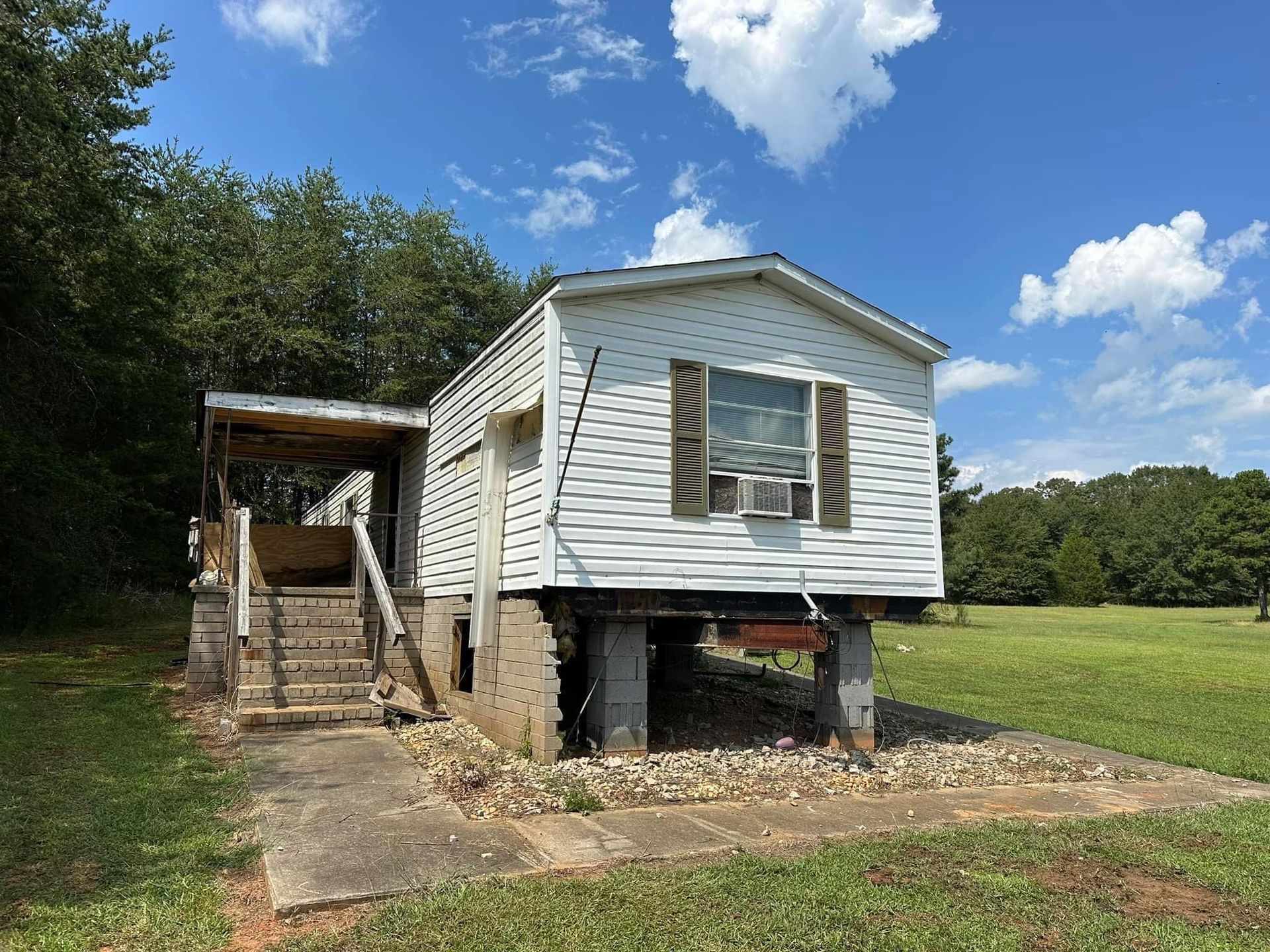 A white mobile home is sitting in the middle of a grassy field.