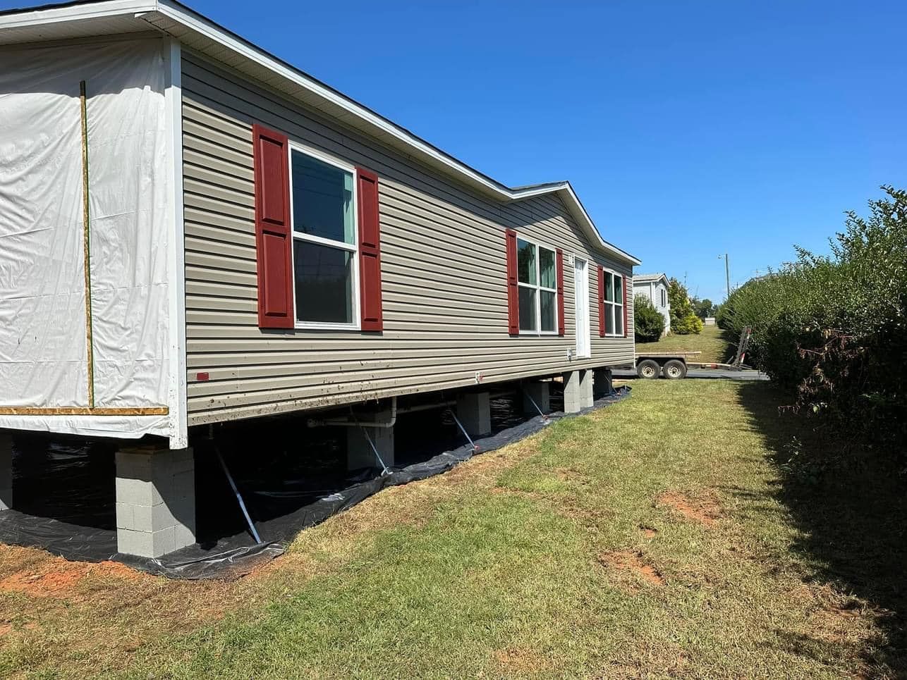 A mobile home is being built on stilts in a grassy yard.