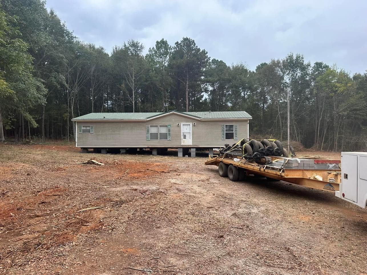 A mobile home is sitting on top of a trailer in a dirt field.