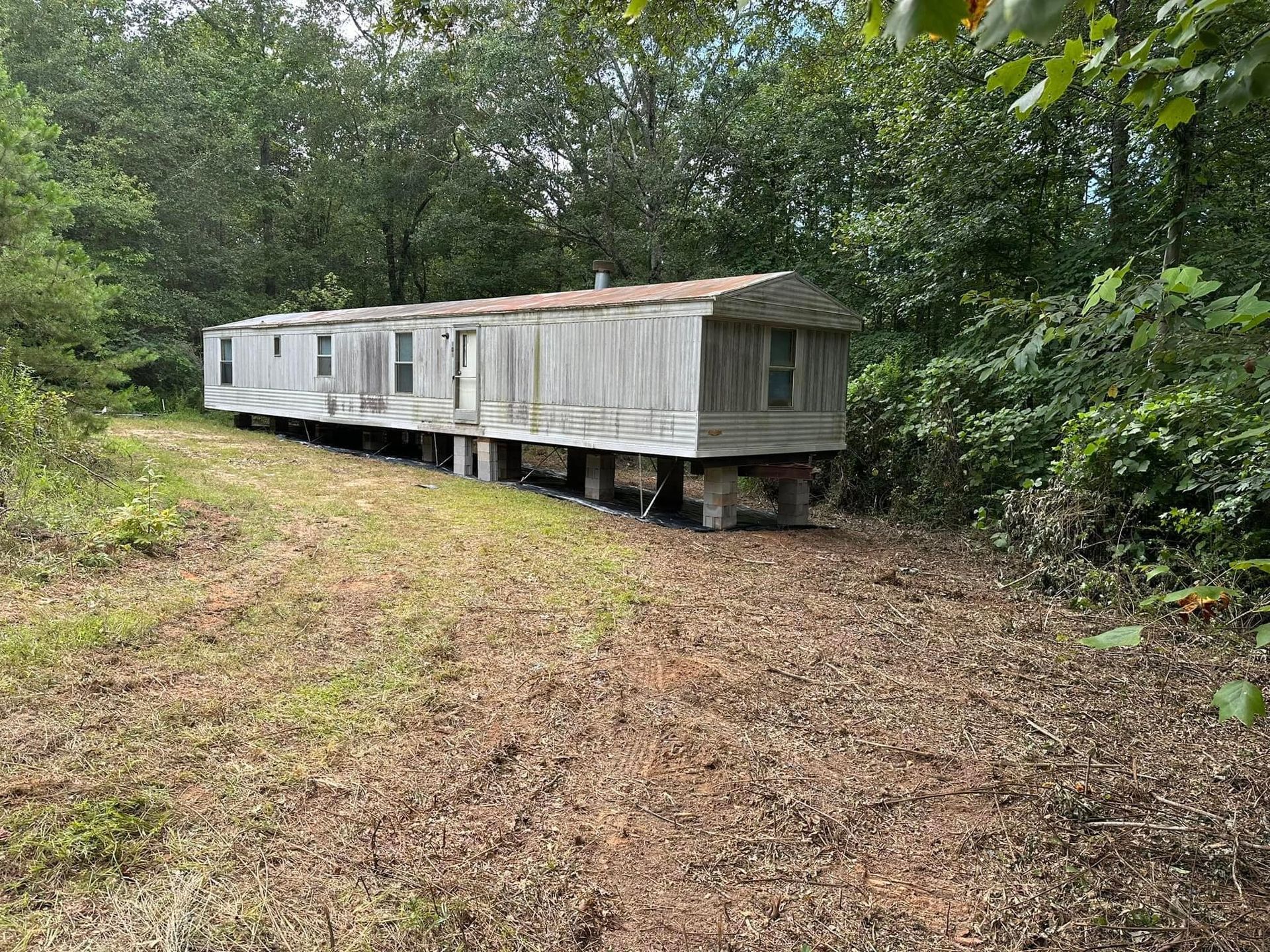 A mobile home is sitting in the middle of a field surrounded by trees.
