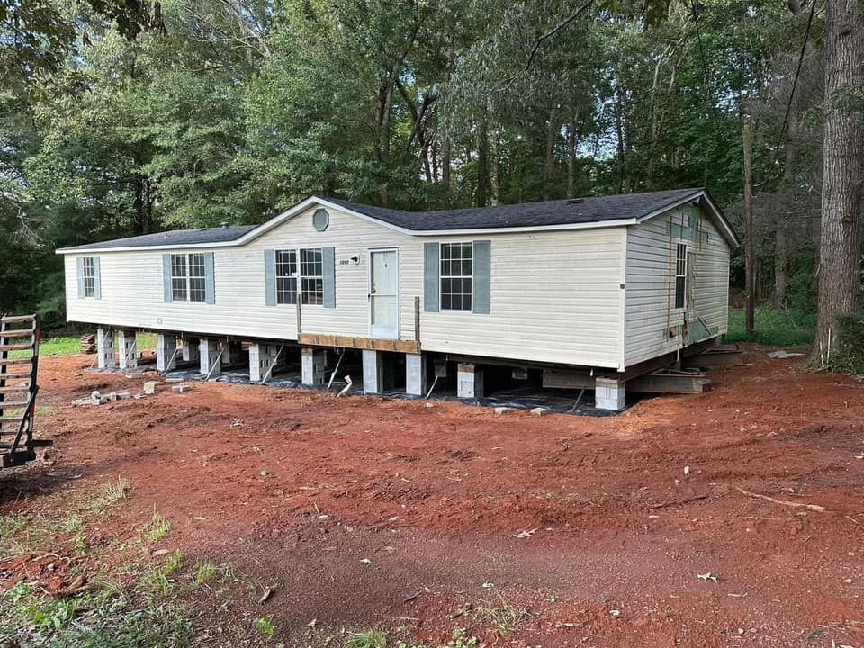 A mobile home is sitting on stilts in the middle of a dirt field.