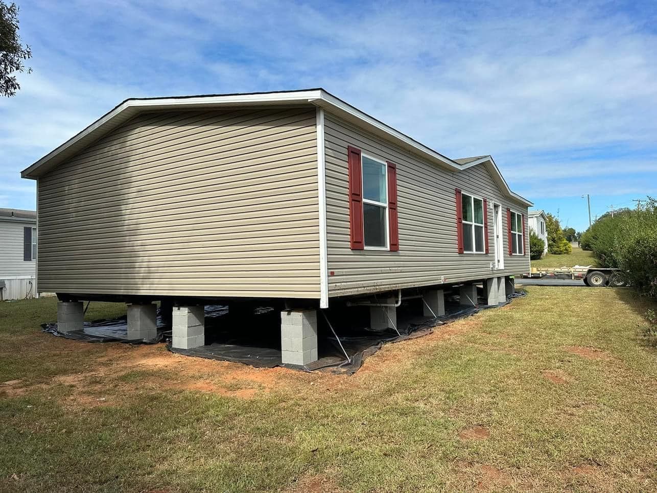A mobile home is sitting on concrete pillars in a grassy yard.