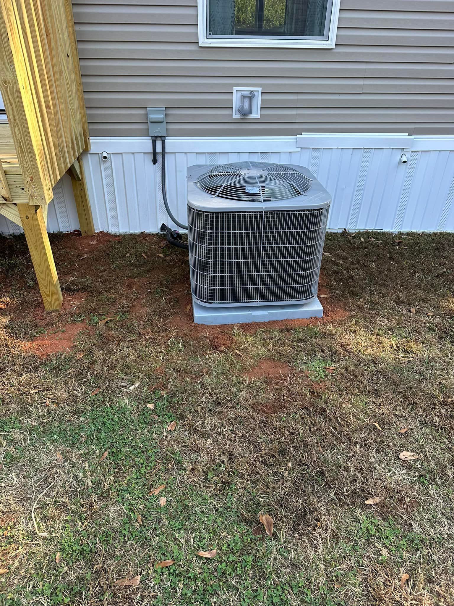 An air conditioner is sitting in the grass next to a house.