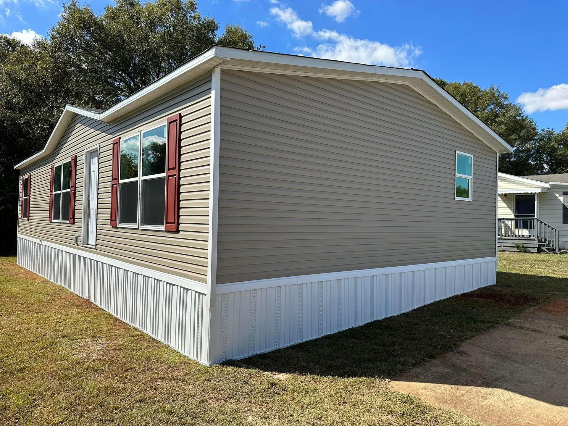 A mobile home with red shutters is sitting on top of a lush green field.