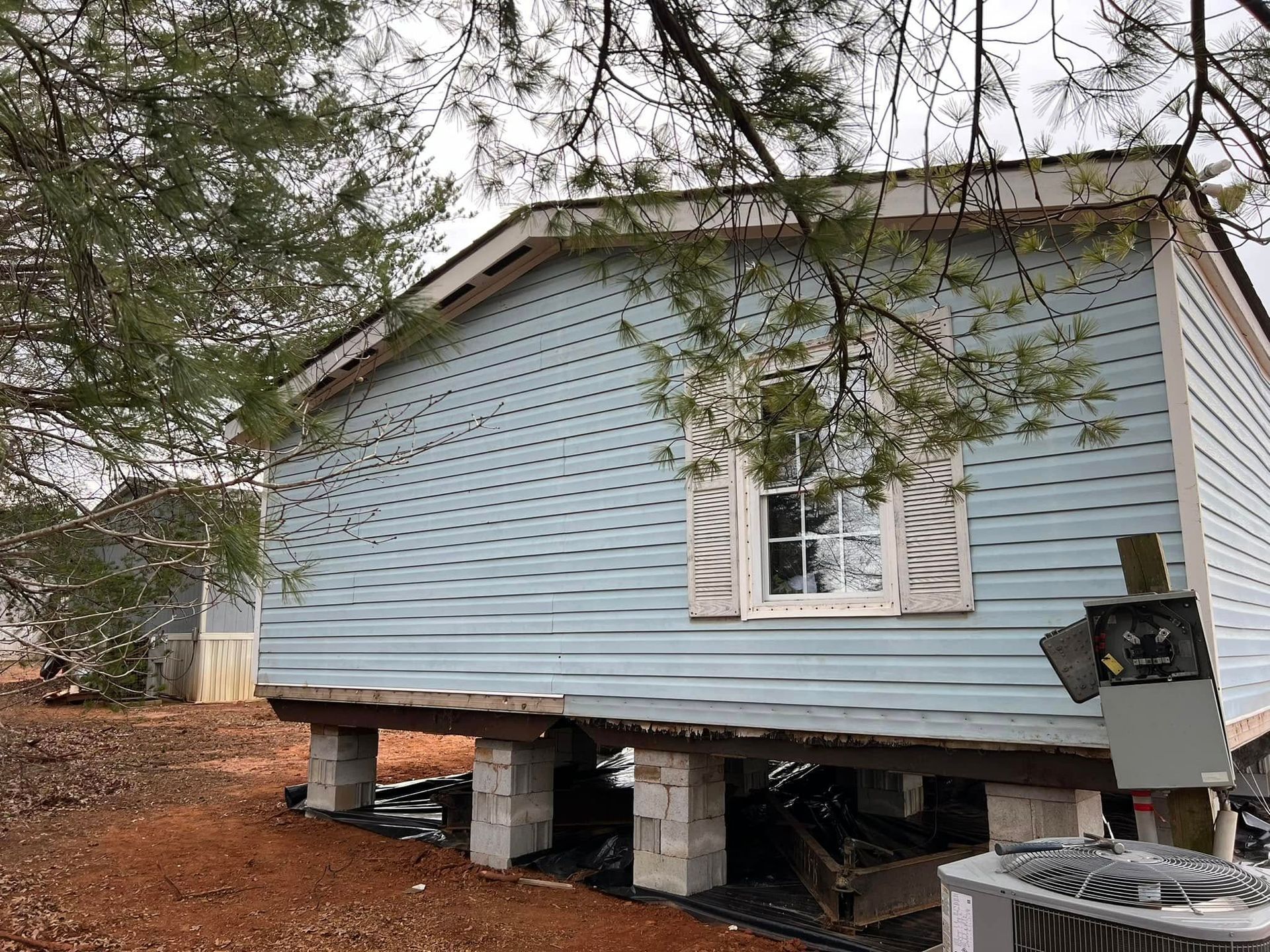 A mobile home is sitting on stilts in the middle of a dirt field.