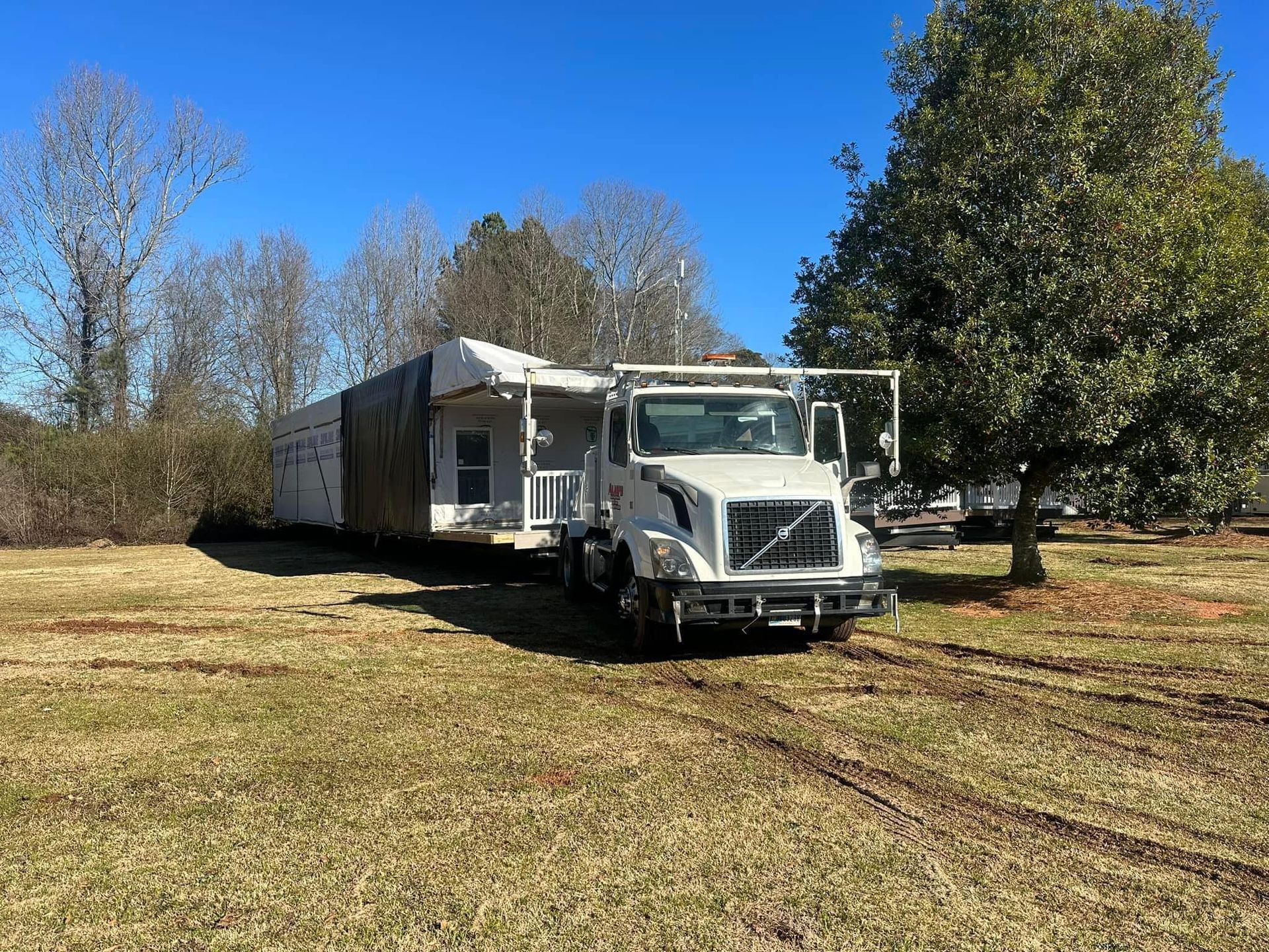 A white truck is parked in a grassy field next to a trailer.