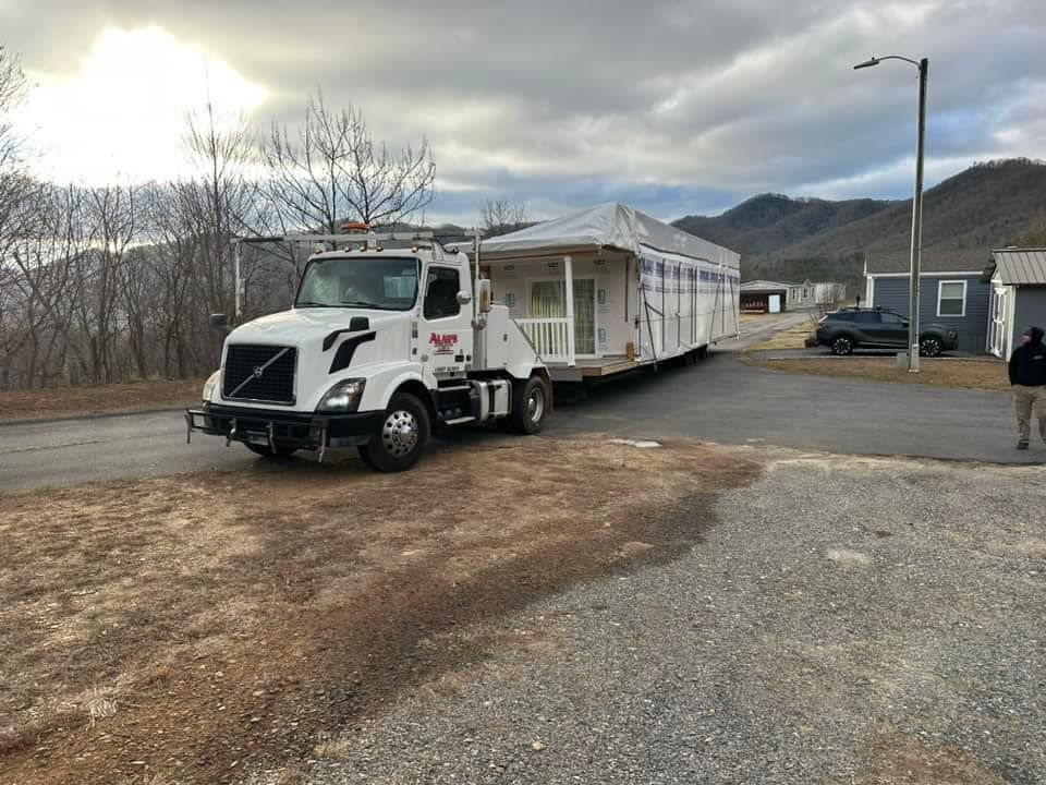 A white truck is carrying a mobile home down a road.