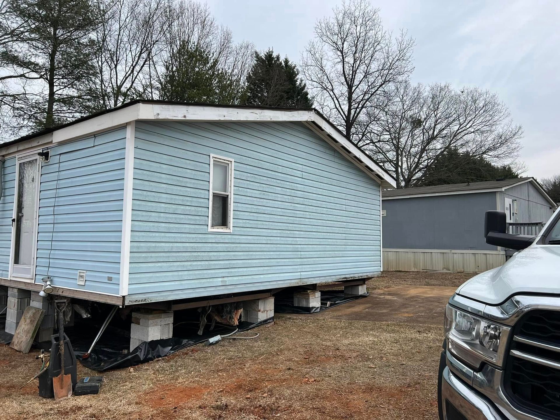 A mobile home is sitting on top of a dirt field next to a truck.