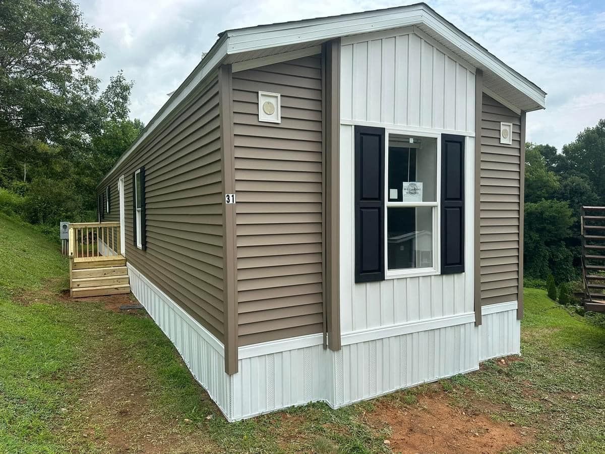 A mobile home with brown siding and white trim is sitting on top of a lush green hillside.