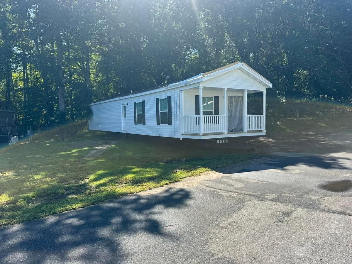A white mobile home with a porch is parked on the side of the road.