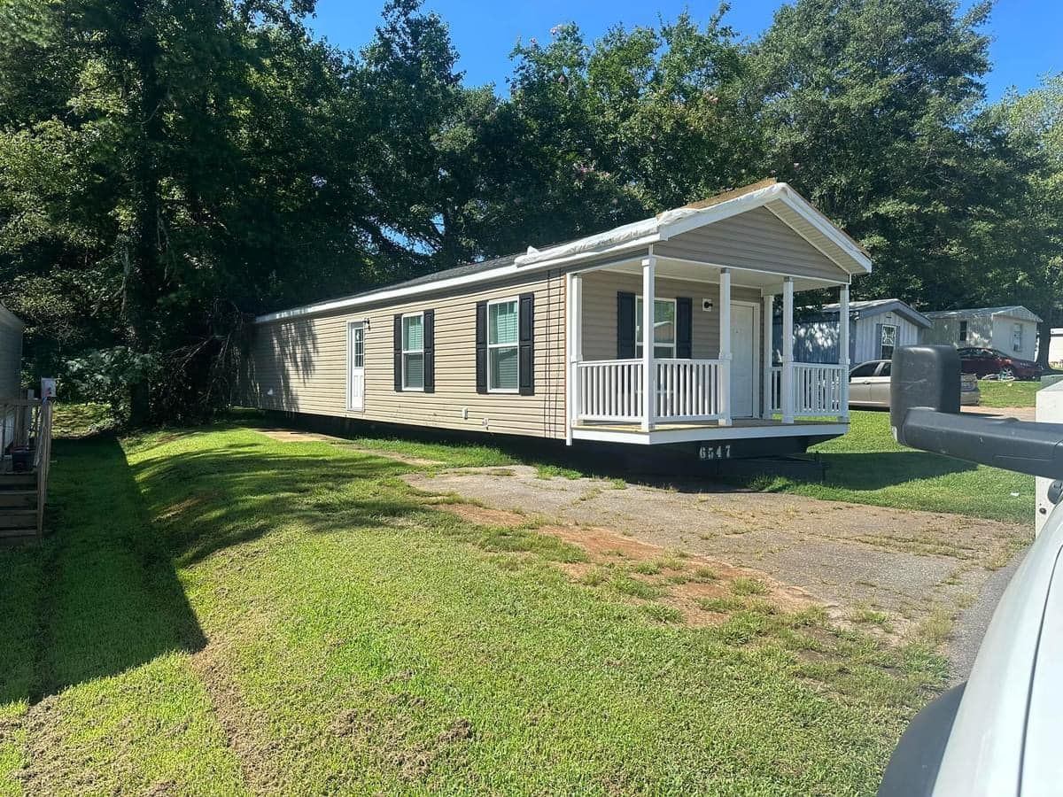 A mobile home with a porch is parked in a grassy yard.