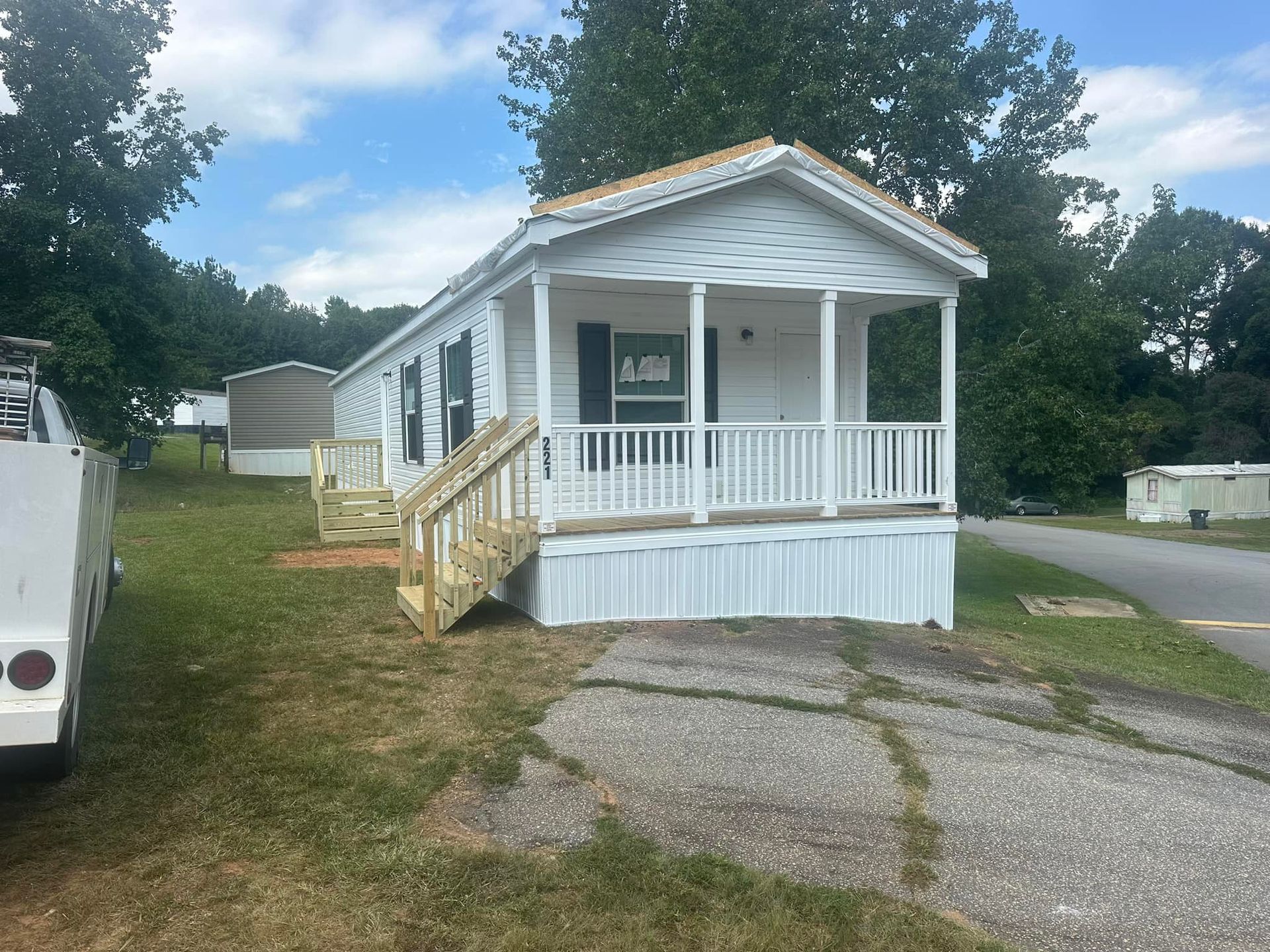 A white mobile home with a large porch and stairs.