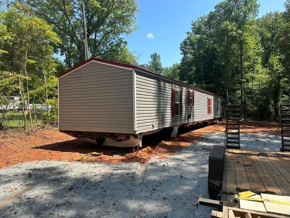 A mobile home is sitting on top of a gravel road next to a trailer.