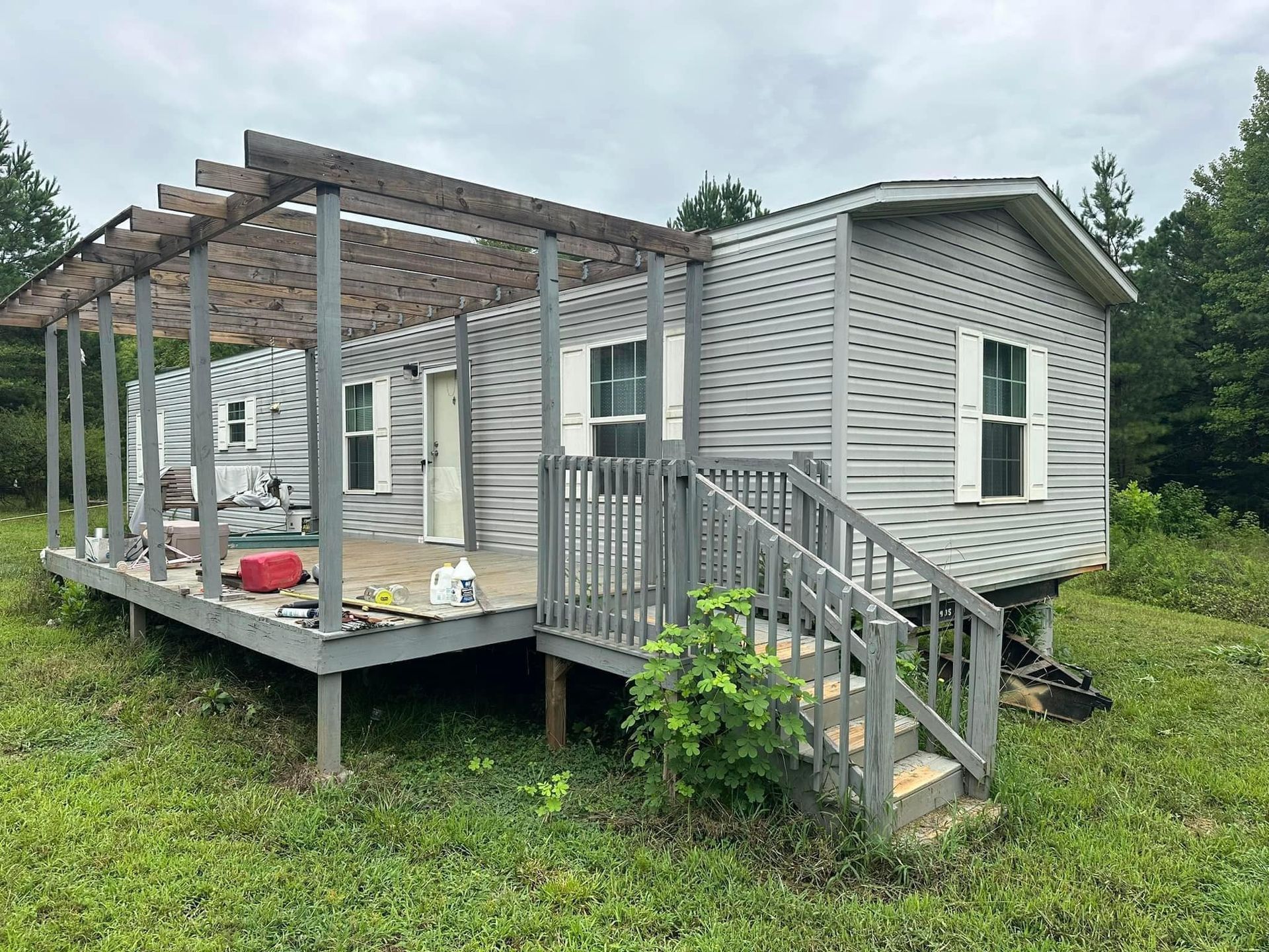 A mobile home with a porch and stairs in a grassy field.
