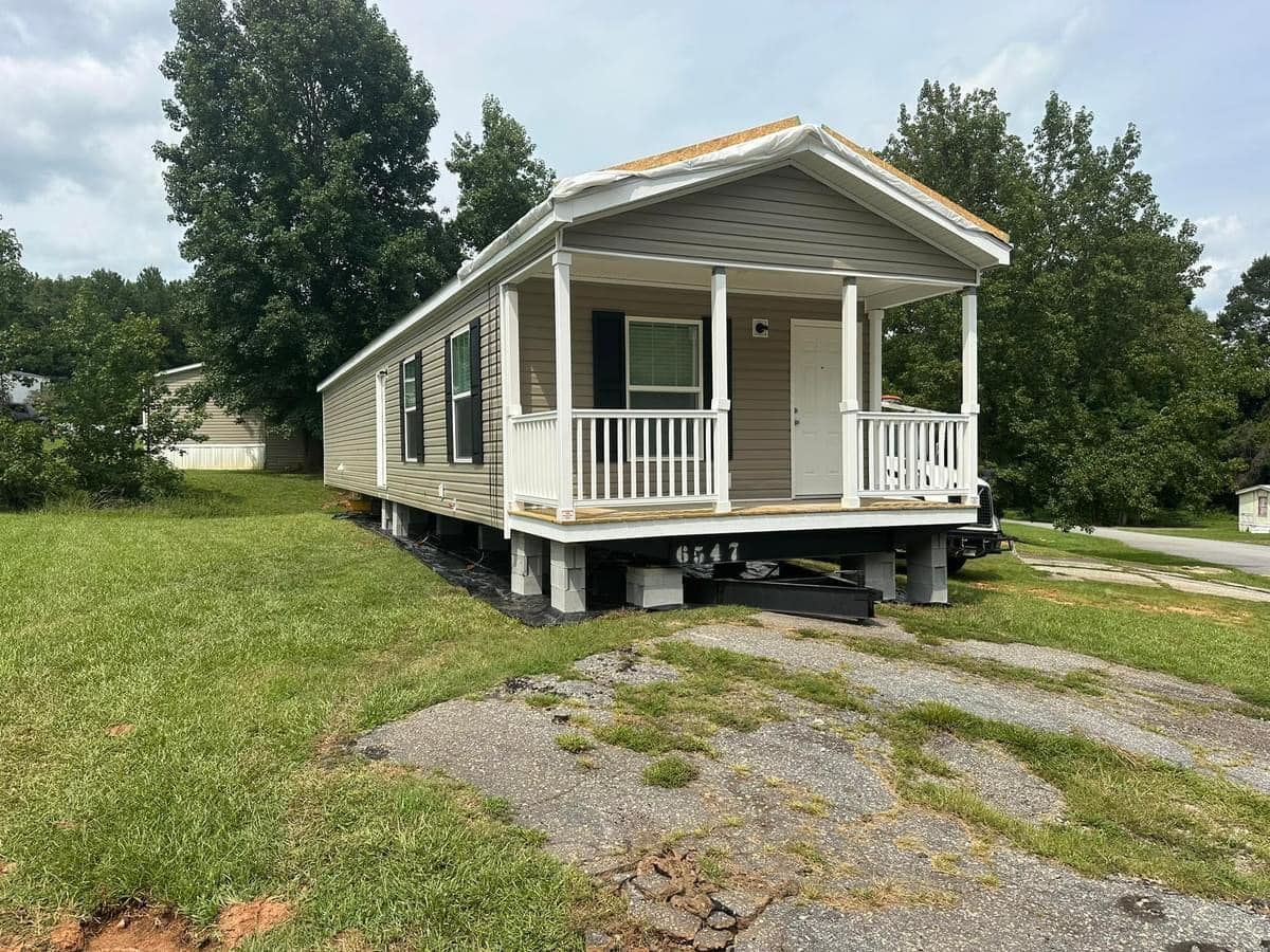 A small mobile home with a porch is sitting in the middle of a grassy field.